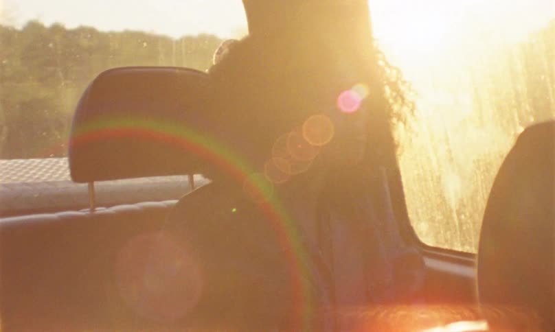 A young woman smiles as she looks out the window from the backseat of a car