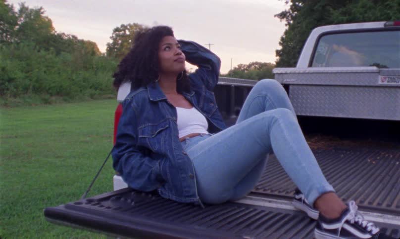 Young black woman relaxing and smiling in bed of pickup truck sitting in field