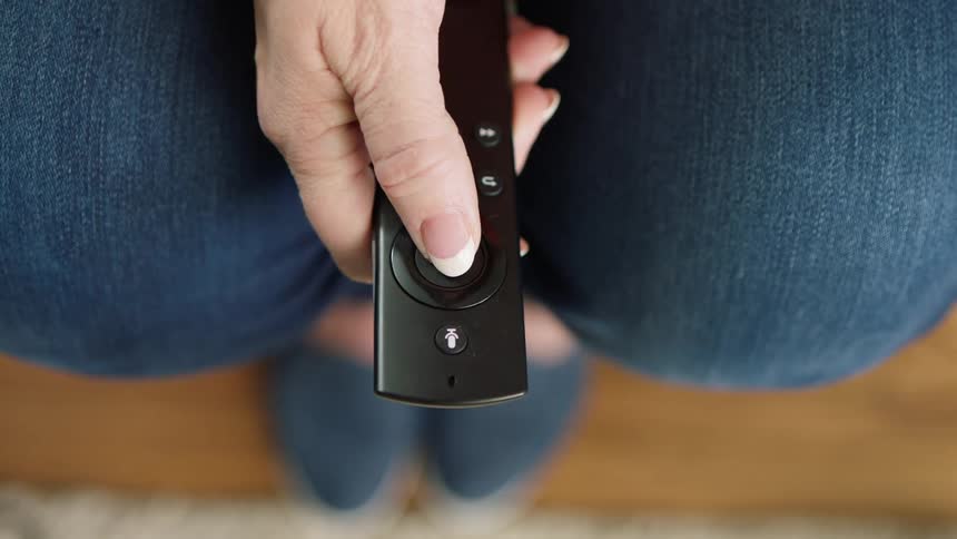 Overhead view female hand pressing button on tv remote