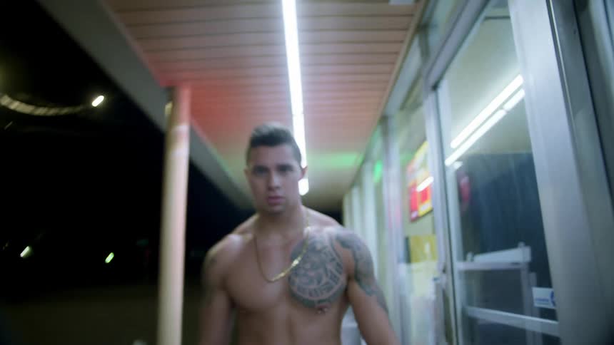 A young man walking down a city street at night without a shirt on
