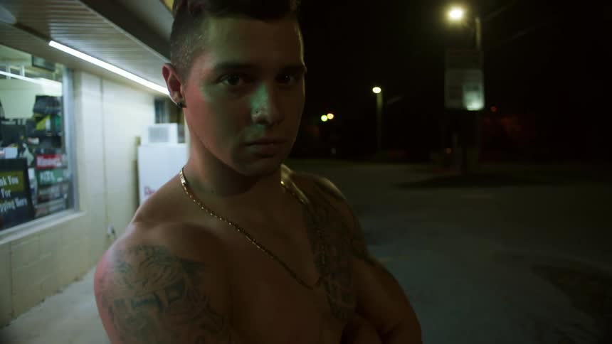 Shirtless teenage tattooed man stands in the streets at night