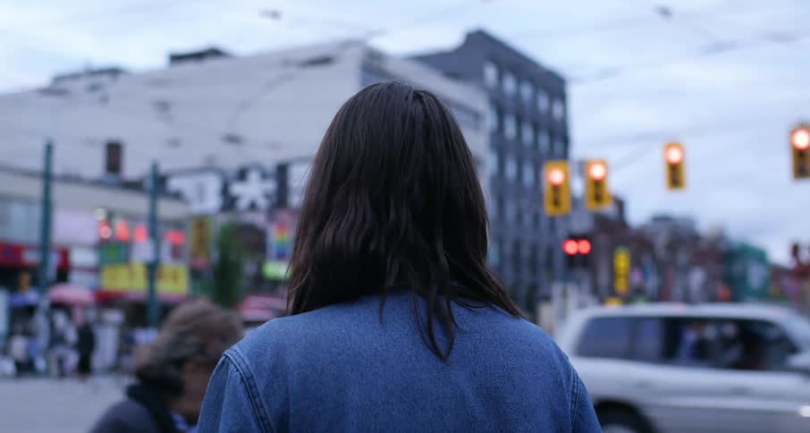 Woman stands at a busy intersection watching pedestrians go by.