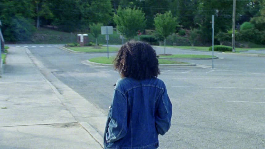 A young woman walks down a sidewalk near a parking lot
