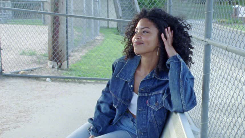 A woman sits on a park bench and flips her hair behind her head with a large smile