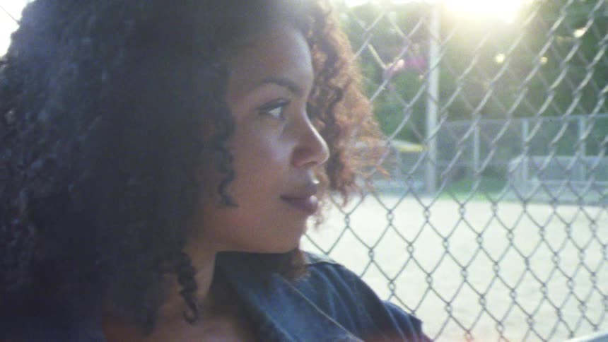 A woman standing next to a chain link fence with trees and the sky in the background