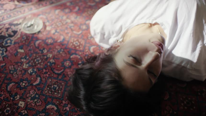 Young woman lies on a rug on the floor smoking a cigarette