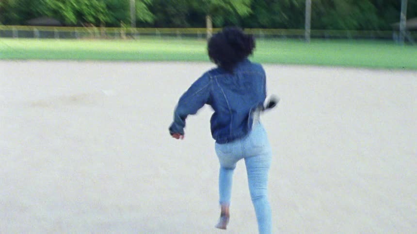 A woman wearing all denim runs from first base to second base on a baseball diamond