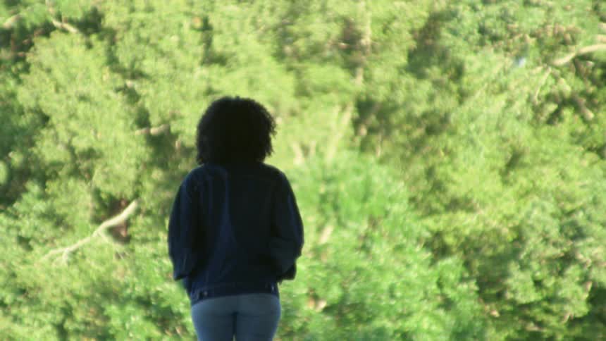 Young woman standing in front of the green folliage of trees
