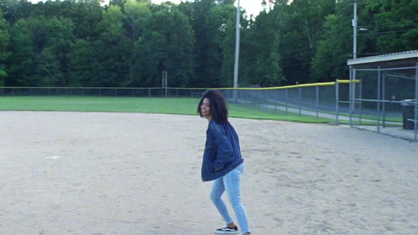 A woman is jogging and skipping across a baseball diamond
