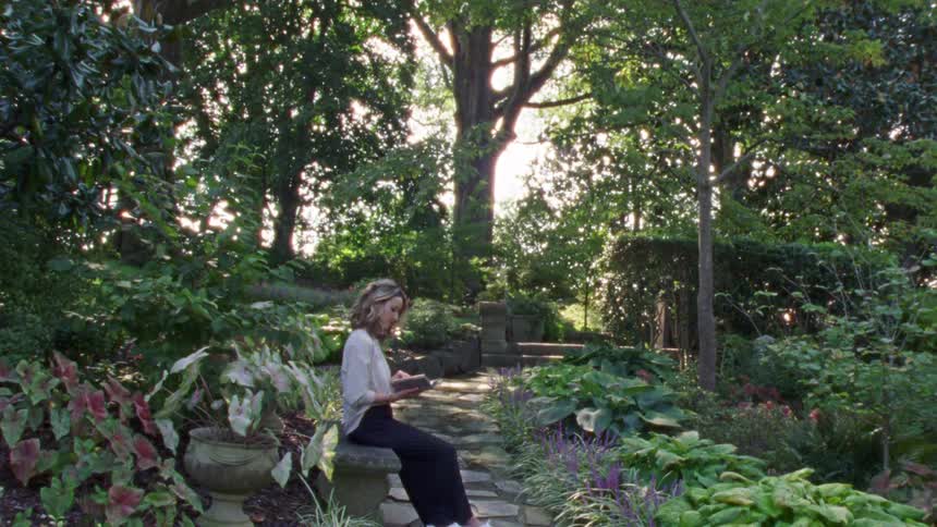 Woman with a white shirt and black pants sitting on a stone bench reads a book in the public park