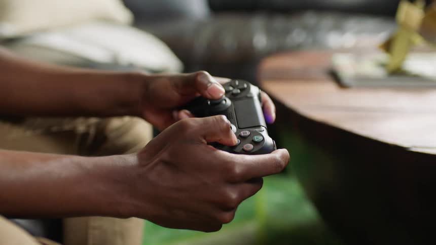 A man sits on his couch and plays video games using a wireless controller