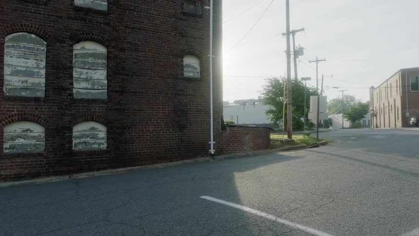 Buildings and trees sit by the empty road under a sunny sky
