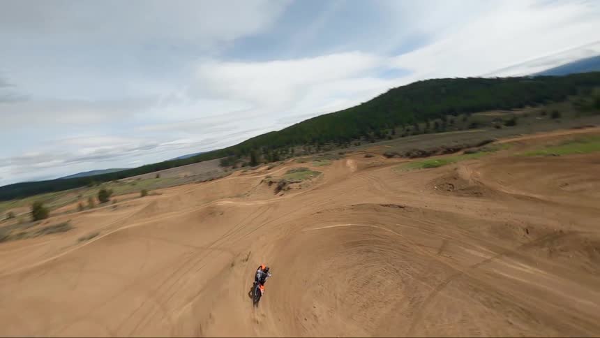 Motorcycle rider rides in a sandy field and jumps the bike over the hills