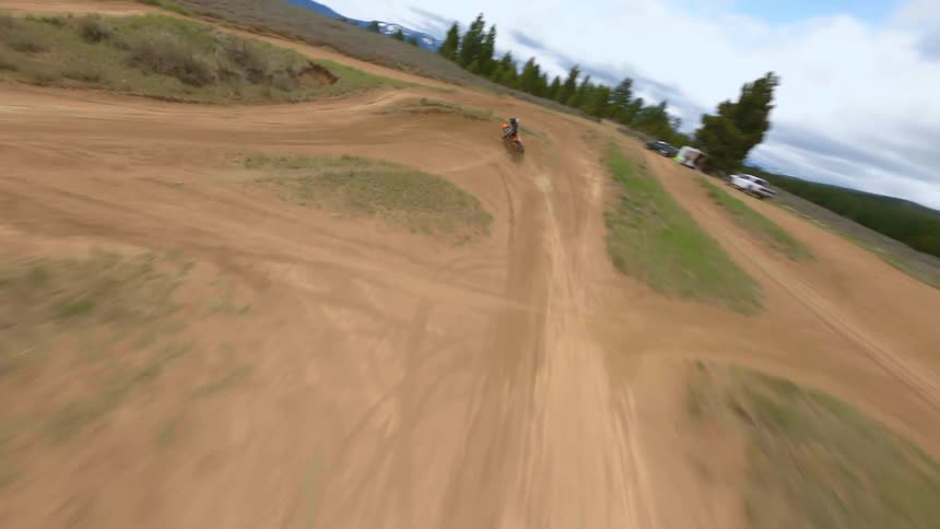 A person riding a dirt bike offroad on a dirt track makes a sharp turn at high speed
