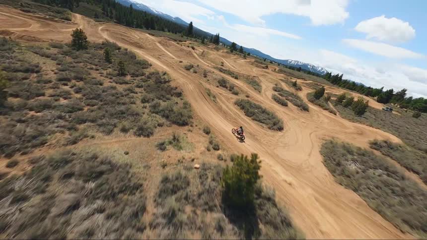 A person riding a dirt bike flies into the air after speeding up a dirt mound on a off road motorcycle track