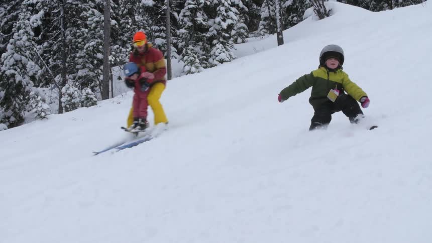 A father skis down a snowy hill with his children
