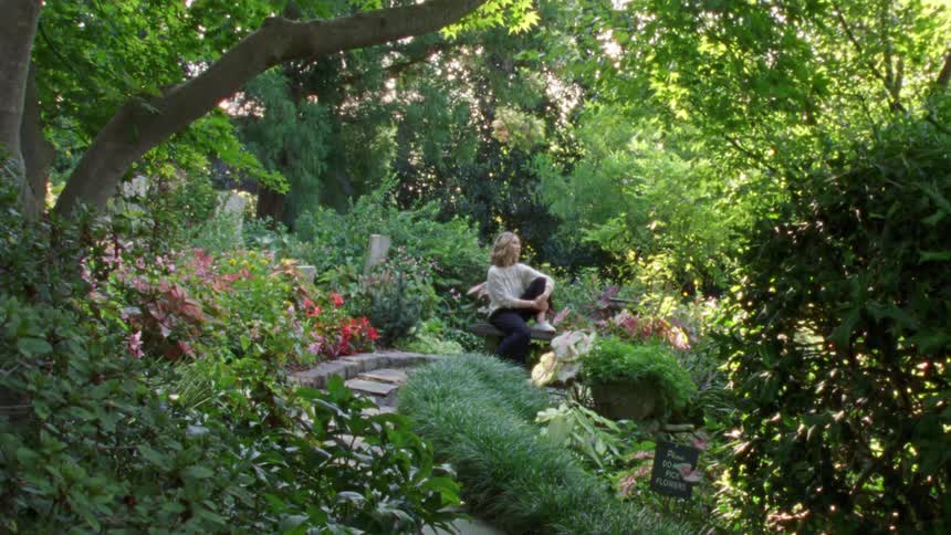 A young woman sits on a bench in a garden