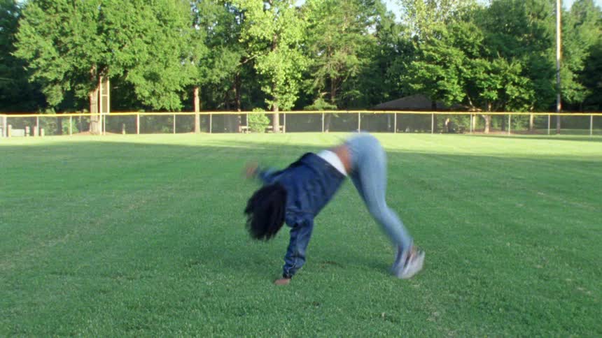 A woman does a cartwheel on a public park grass field