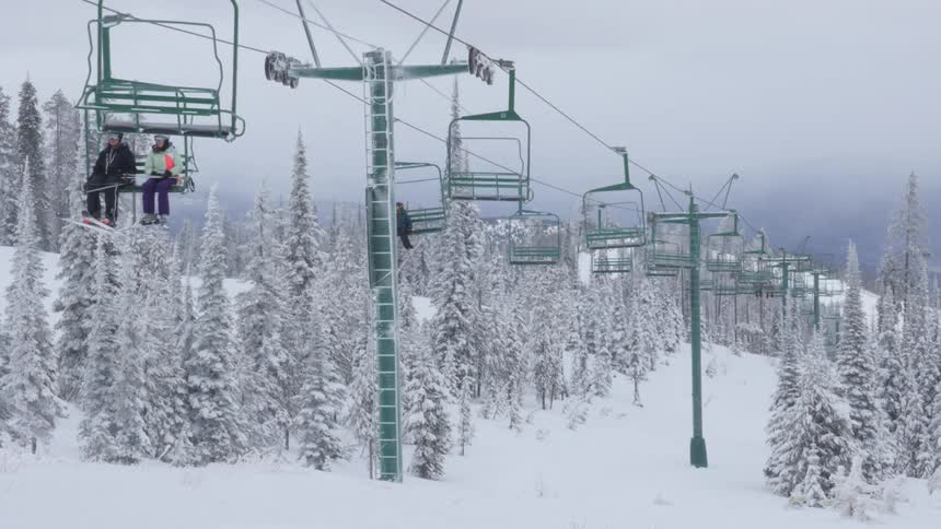 Skier skis down a hill while a ski lift carries skiers overhead