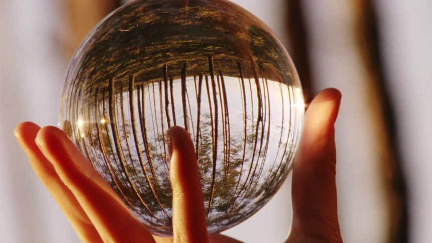Trees reflect off a clear crystal ball that a woman holds and spins in her hand in the forest