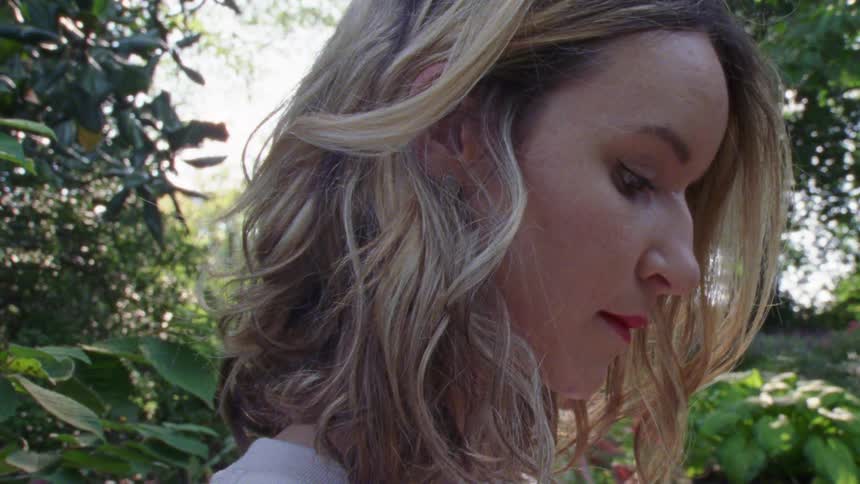 A white woman stands outdoors in a garden
