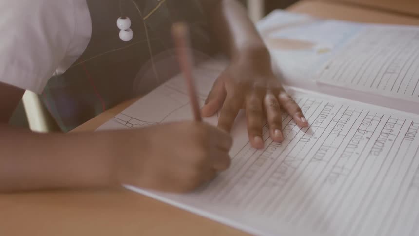 A young girl sits at a desk writing in a school workbook
