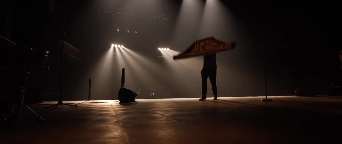 A man walking with a carpet on a stage then spreading it on the stage floor