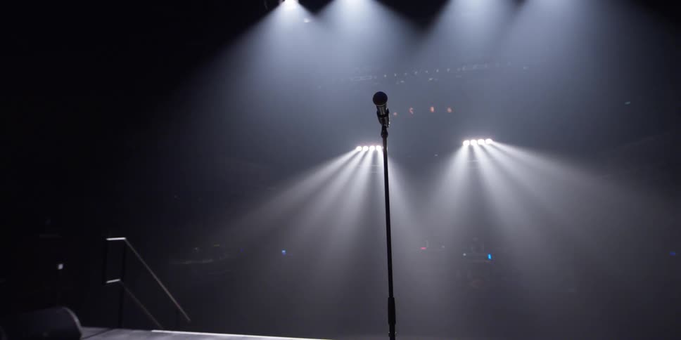 A microphone and stand sit on a stage lit up by lights at the back of a theater