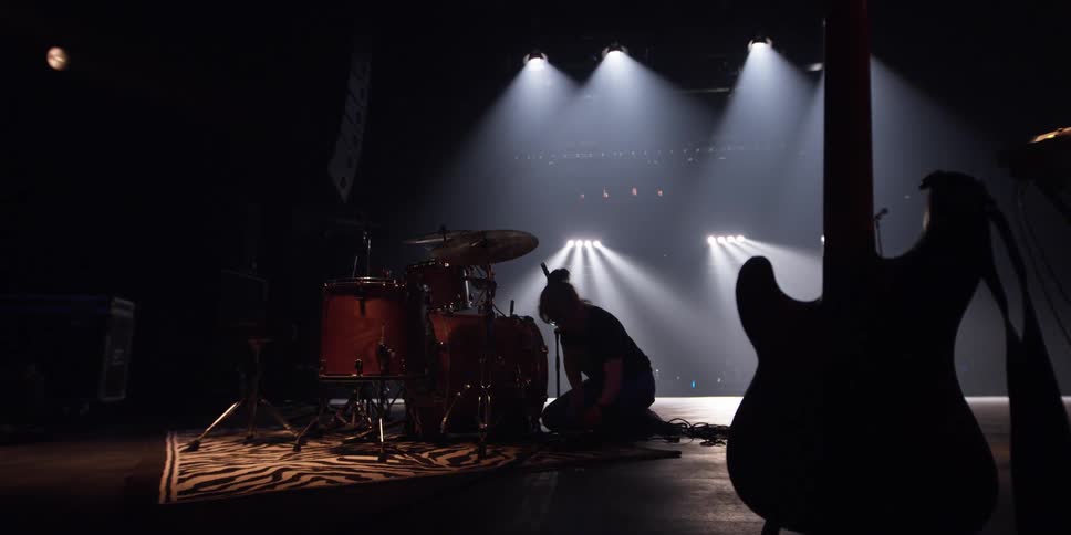 A stage hand connects cables on a drum set