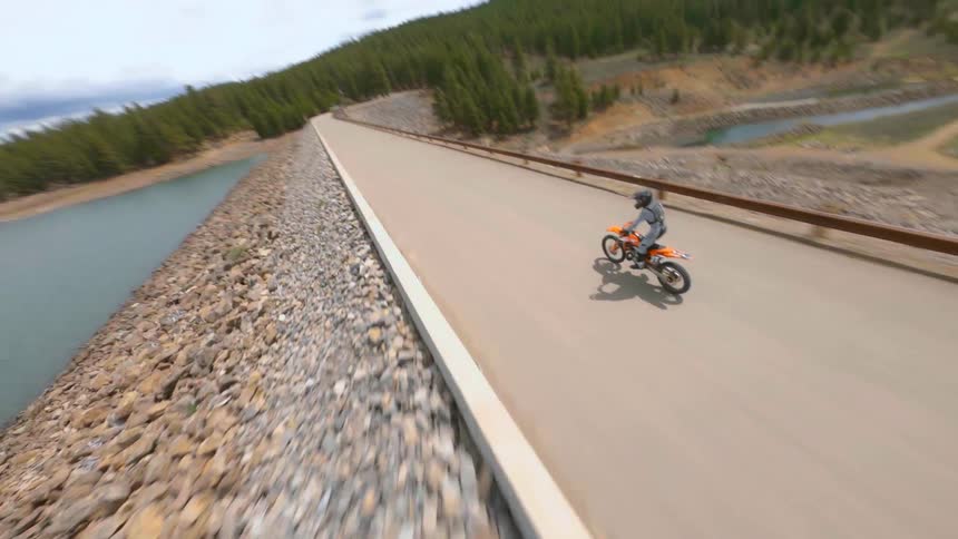 A person in a dirt bike riding on a road popping a wheelie with trees and the sky in the background