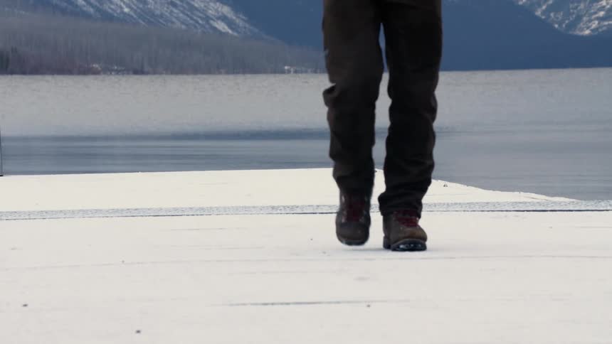 Pedestrian walks on the dock near the lake as snow sits on the mountains