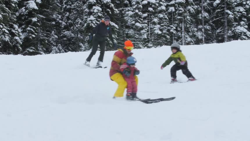 A mother and father ski down a hill with their small children