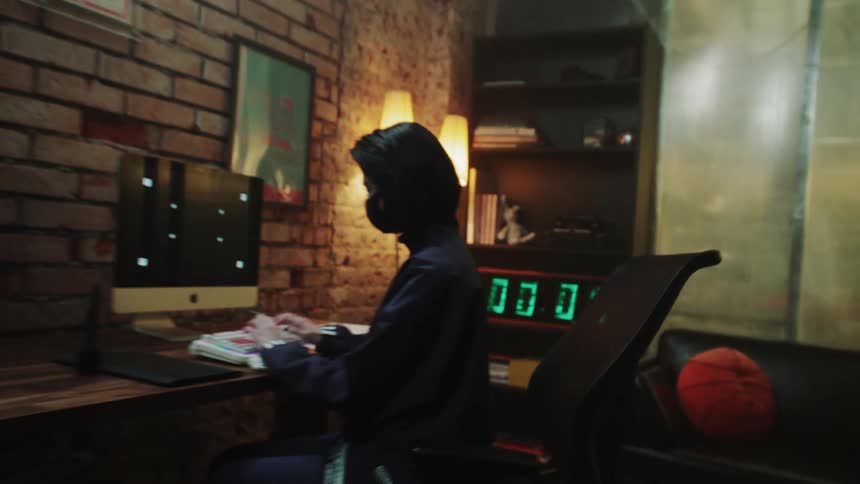 Woman types on a keyboard while sitting at a desk as a bookshelf stands nearby