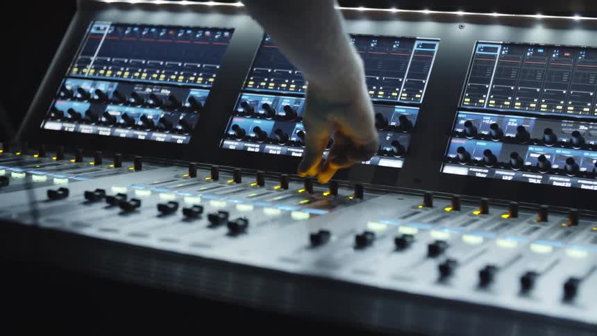 A white man adjusts dials and switches on a large sound board