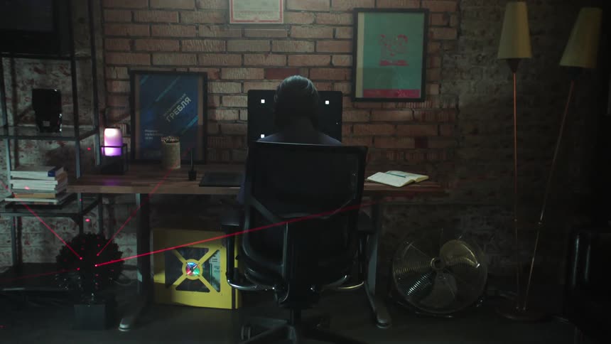 A person sits at a computer desk with a disco style laser light flashing around the room