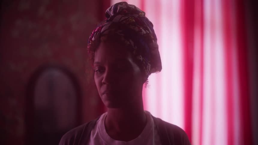 Black woman wearing a colorful hat stands in front of pink curtains