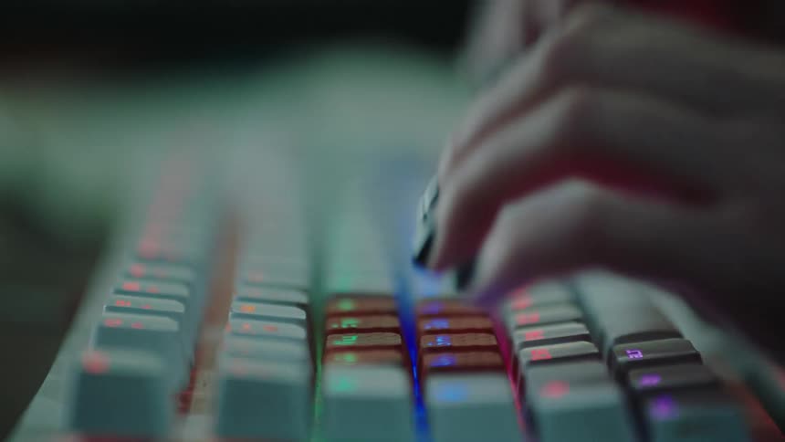 Woman with manicured nails types on a white rgb back light keyboard