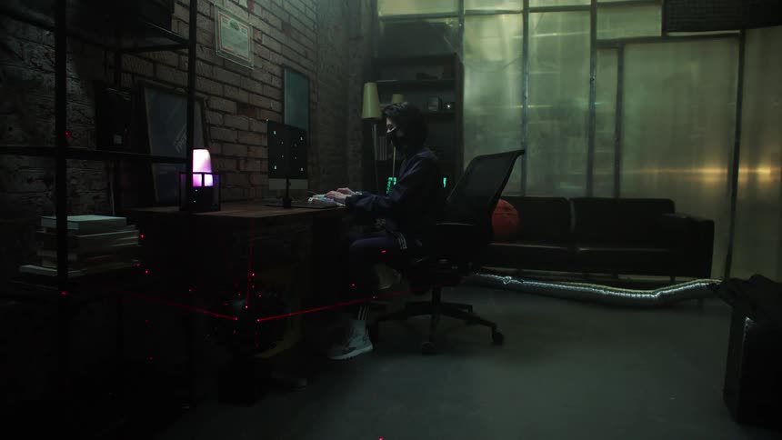 A young woman sits at a desk and types as she controls a robot on the floor