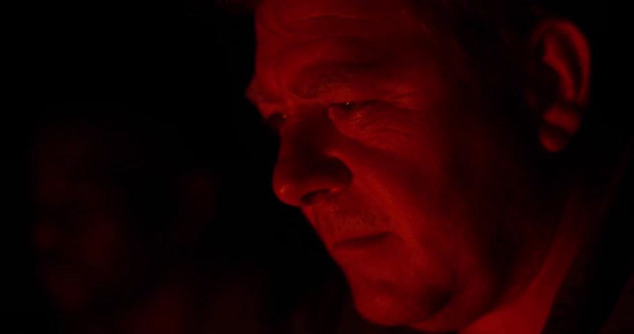 Close up of a mans face looking at the flames of a camp fire at night