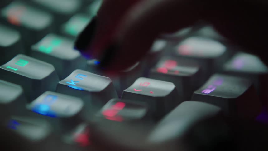 Woman with painted fingernails types on a keyboard that has colored symbols on the keys