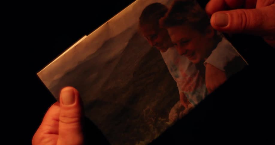 A person holds a picture of two young men in a dark room