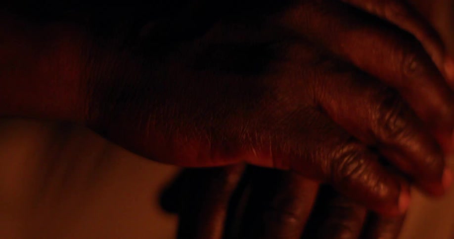 A black man rubs his hands together in flickering light
