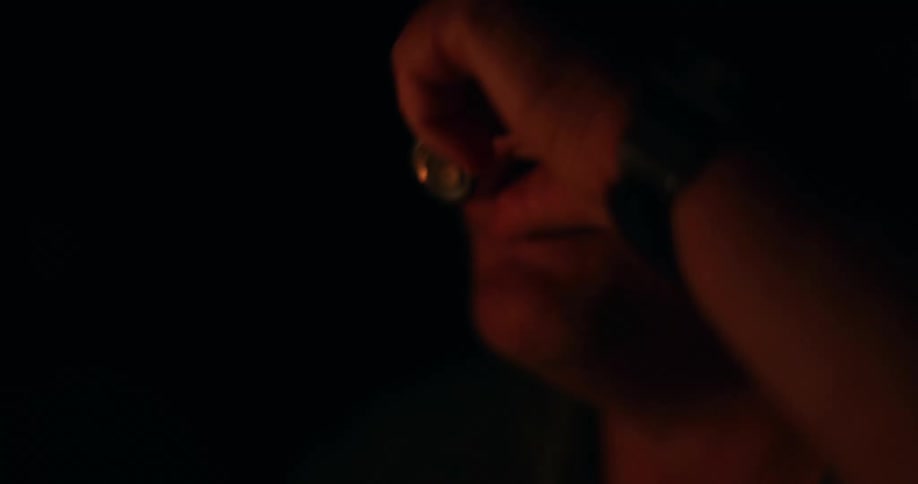 Man sits in dark room lit by flickering firelight while drinking
