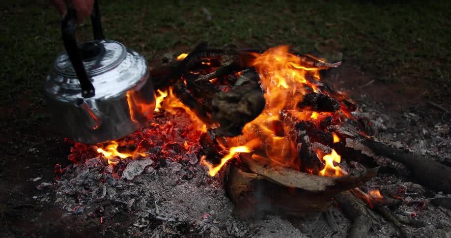 A man puts a kettle over an open flame outside