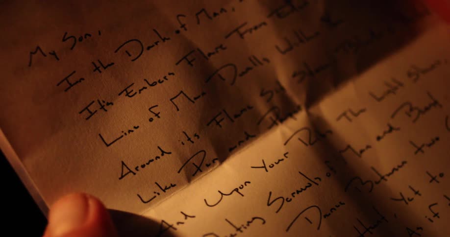 A person holds a creased hand written letter in a dimly lit place