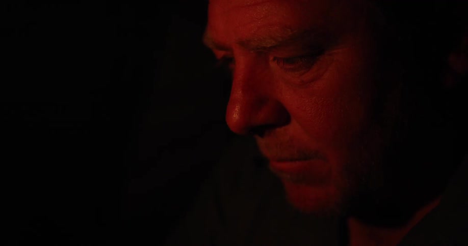 Middle aged man in deep thoughts watches a campfire at night