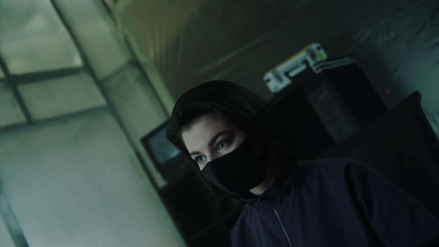 A woman in a face mask sits before a computer typing on a keyboard with illuminated keys