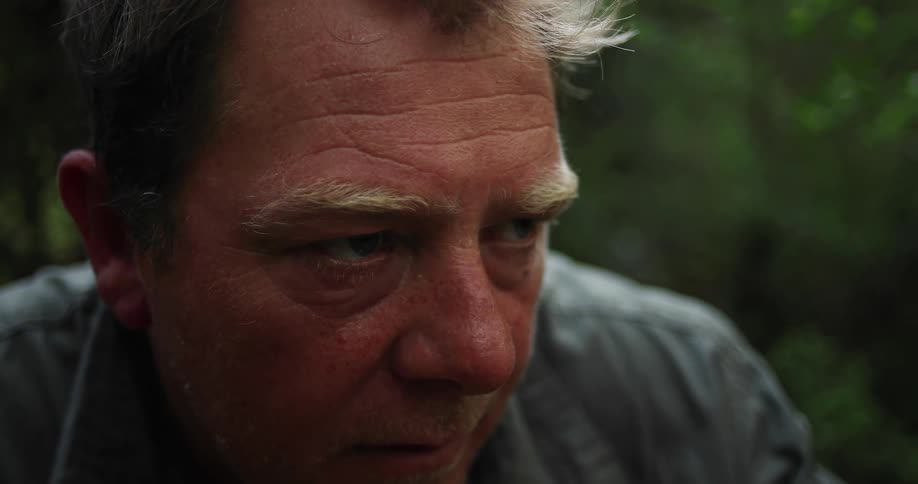 Elderly man stares into the distance while trees sit nearby