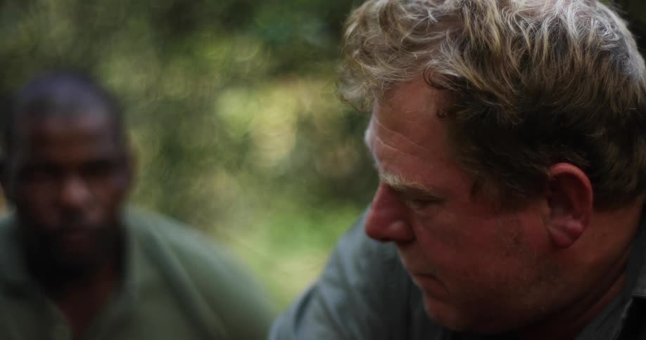 Men in the forest look at each other before shooting a shotgun