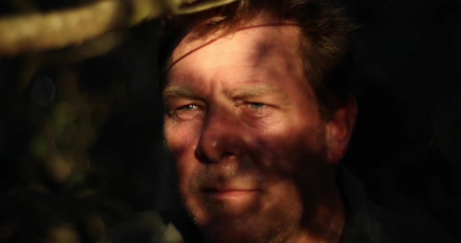 Shadows move across a mans face as he stares ahead